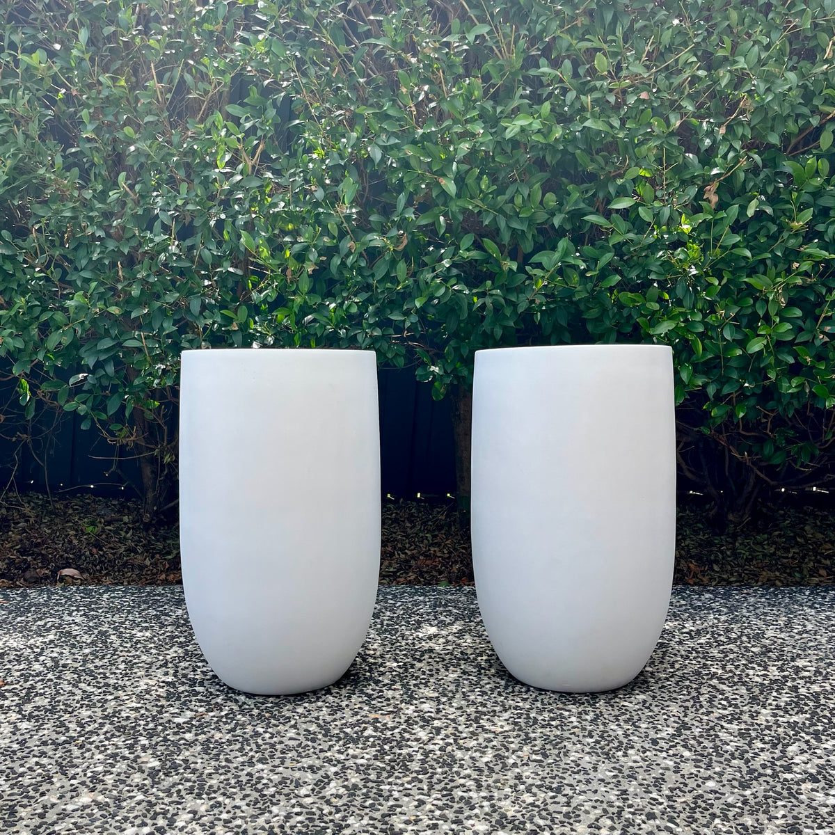 Pair of pure white false bottom tall U-pots displayed outdoors on gravel