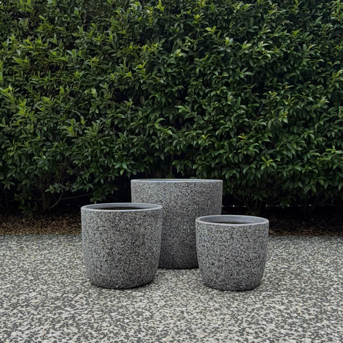 Pair of Prague Grey Pebble round curved garden pots displayed against green hedge