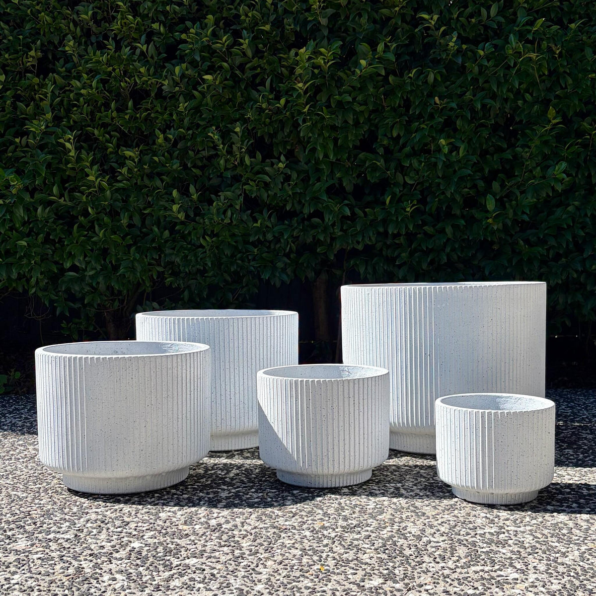White terrazzo fluted footed cylinder planters cluster displayed outdoors on gravel
